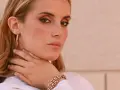 Donna con lentiggini e gioielli in oro rosa, un bracciale a maglie larghe e orecchini a cerchio.