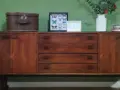 Mobile legno scolorito con cassetti e ante, decorato con una valigia vintage, cornici con farfalle e un vaso di fiori.
