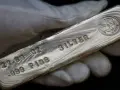 Mano guantata tiene un lingotto di **titolo argento** 999.9, con incisioni che indicano 27.00 oz e "FINE SILVER".