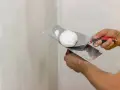 Mani che usano spatole per applicare stucco su un muro. Lo stucco serve a livellare e riparare le imperfezioni.