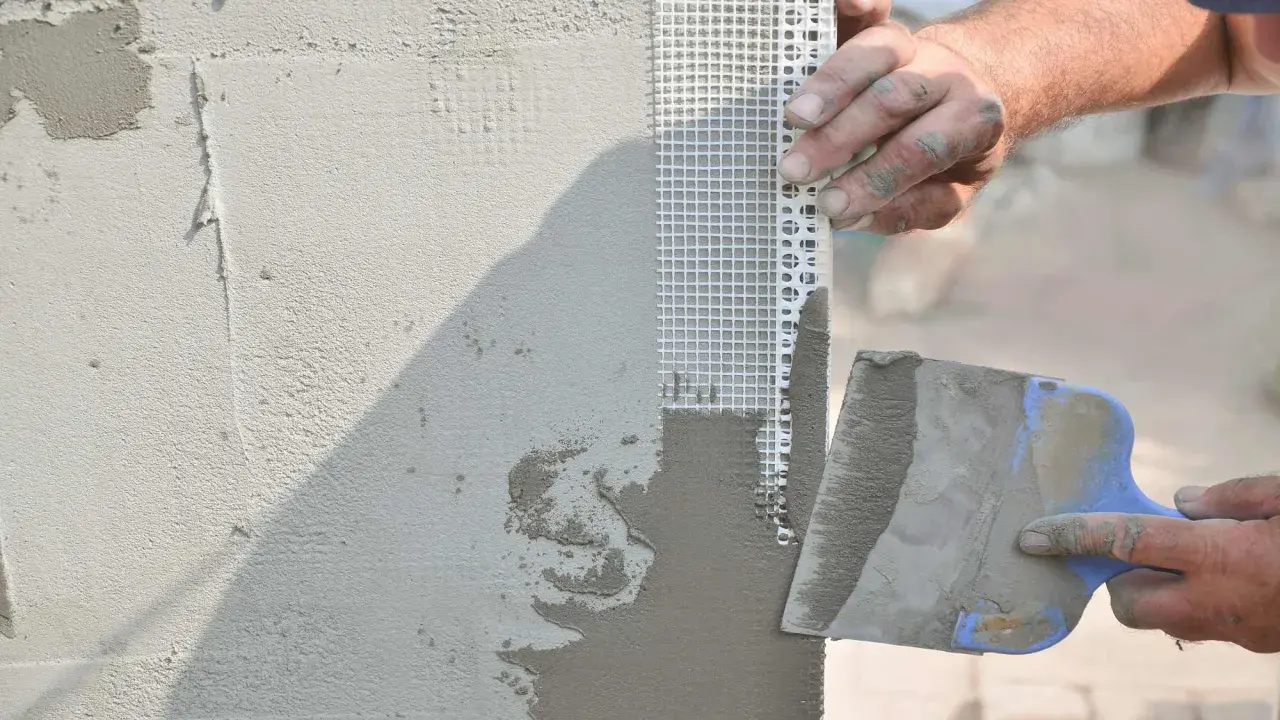 Mani esperte applicano stucco e rete per stuccare angolo muro, garantendo una finitura perfetta.
