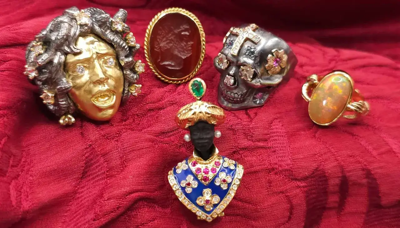 Gioielli unici: un volto dorato, un teschio tempestato, un cammeo e un busto con pietre preziose, un anello con opale e un altro con un prezioso oro rosso.