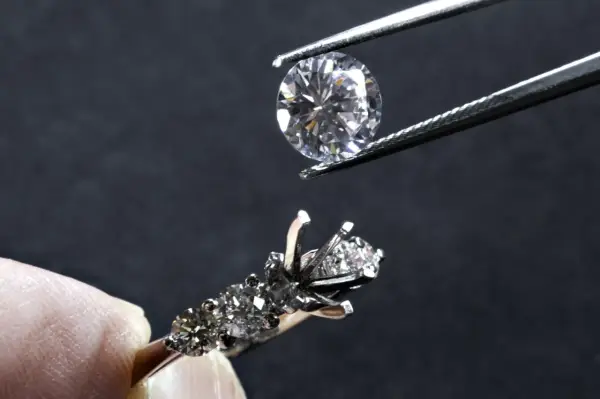 Un diamante viene posizionato con una pinzetta su un anello con incastonatura a castone ribattuto, pronto per essere fissato.