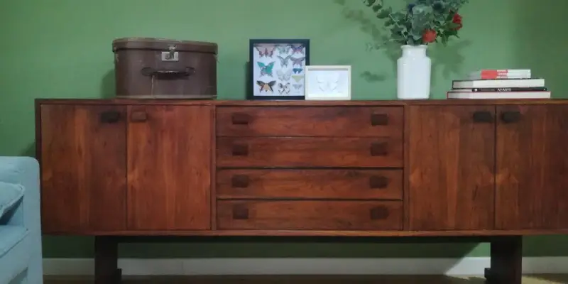 Mobile legno scolorito con cassetti e ante, decorato con una valigia vintage, cornici con farfalle e un vaso di fiori.