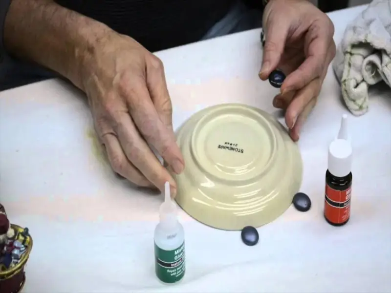 Mani che lavorano per riparare la ceramica con colla e piccoli pezzi.
