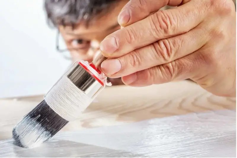 Un uomo applica il primer per legno con un pennello, preparando la superficie per la verniciatura.